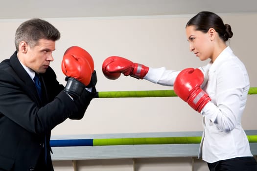 Portrait of aggressive businessman in boxing gloves with serious female opposite him