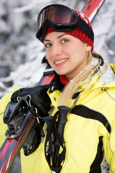 Sporting young beautiful woman with skies on the background of snow-covered forest