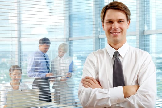 Business leader looking at camera with team of partners working in office behind