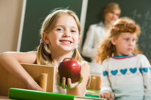 Portrait of happy pretty girl holding a red apple in the classroom