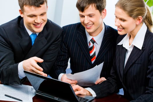 Portrait of three young specialists looking at monitor of laptop