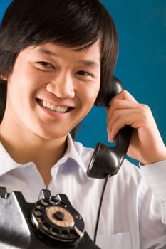 Image of happy Asian man holding telephone receiver and smiling