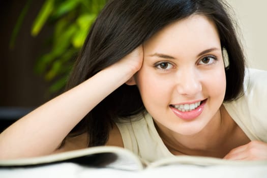 Face of charming female looking at camera with smile while reading a book