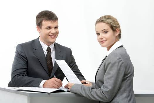 Photo of friendly secretary sitting at table and looking at camera with her partner near by
