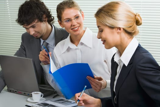 Group of three young business people gathered together discussing an interesting idea in the office
