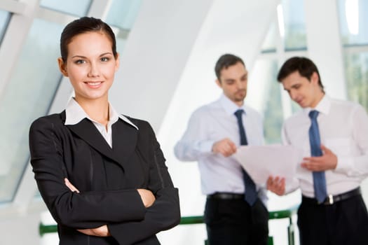 Portrait of attractive business lady looking at camera with smile on background of interacting men