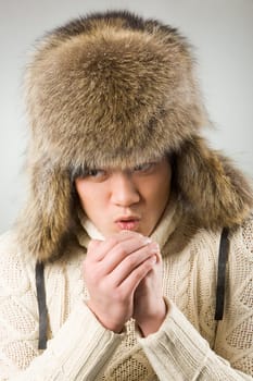 Portrait of cold man in fur hat and knitted sweater warming up his hands