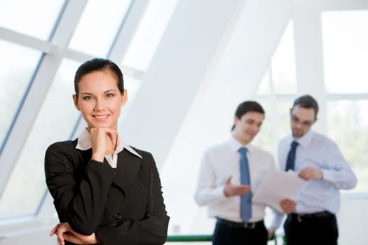 Portrait of attractive business lady looking at camera with smile with men discussing ideas at background