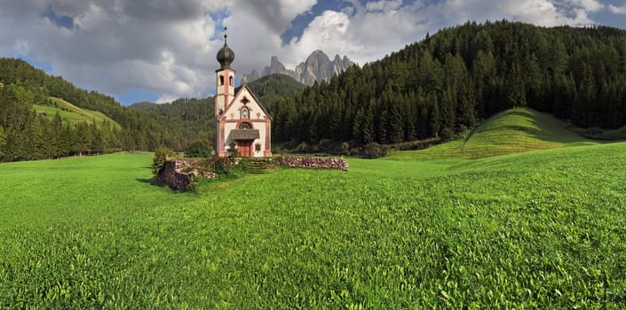 Small Church of St. John in Ranui with Odle Mountains and a dramatic cloudy sky,Funes Valley,Dolomites,Suedtitol,Italy
