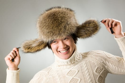 Portrait of happy man in warm fur hat and white sweater having fun