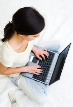 Above view of female student sitting on bed and typing on laptop keypad