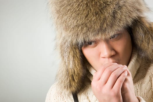 Portrait of cold man in fur hat and knitted sweater warming up his hands