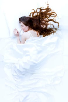 Above view of young beautiful woman sleeping in bed covered with white silky sheet