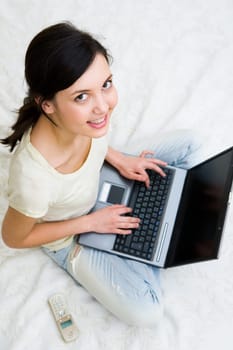Cheerful teenage looking upwards at camera while doing computer work on bed