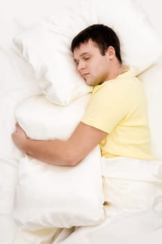 Photo of handsome man sleeping and holding soft white pillow