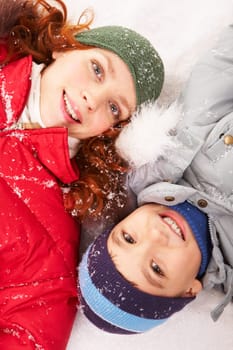 Happy boy and his mother lying in snow and looking at camera