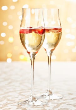 Festive champagne flutes filled with sparkling wine and floating strawberries with a backdrop bokeh of romantic twinkling party lights