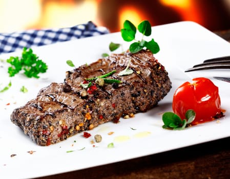 Serving of grilled beef steak coated in hot peppercorns and garnished with fresh herbs and a tomato