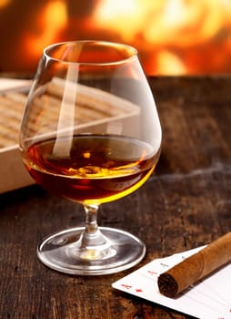 Goblet of cognac warming in front of the fire on a poker night with four aces and a cigar