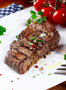 Thick portion of succulent tender peppered steak grilled to perfection and served on a plate with fresh herbs and tomatoes