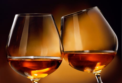 To clink two glasses of Cognac or Brandy liquor in front of a brownish background.