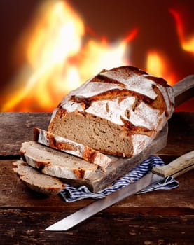 Sliced fresh rye bread on a rustic wooden table in front of a roaring fire