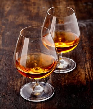 Two goblets of brandy warmed by the glow of the lights on wooden counter top while entertaining a special friend