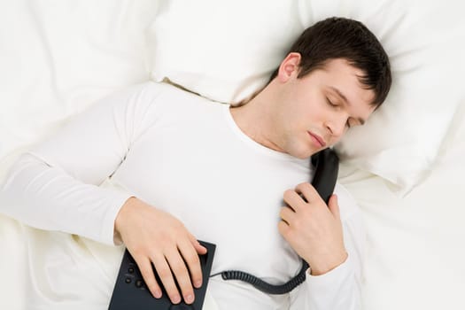 Image of handsome man having rest in bed with telephone in hands