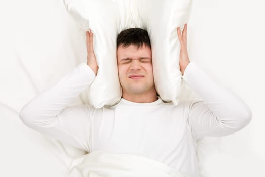 Image of man suffering from insomnia and shutting ears with cushion