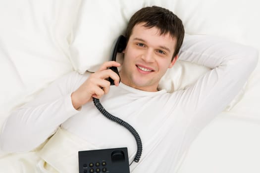 Above shot of smiling man speaking on the phone in bed and looking at camera