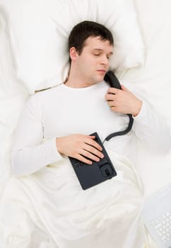 Photo of napping male with telephone in hands and laptop keyboard near by