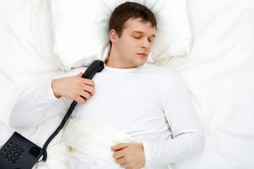 Image of handsome man having rest in bed with telephone near by
