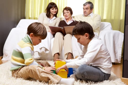 Family of grandparents and mother sitting on sofa and reading and two boys playing together