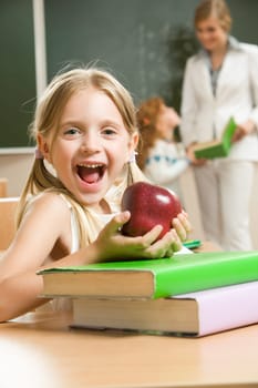 Portrait of happy schoolgirl and apple in her hands sitting at the table with books