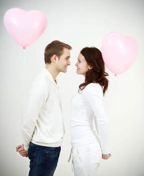Two beautiful young people with heart-shaped balloons looking at each other