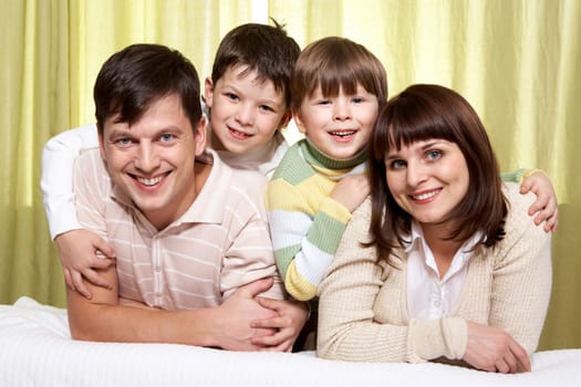 Young parents ant two sons embracing them, looking at camera and smiling