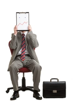 Portrait of stressed businessman sitting on armchair hiding his face with paper showing bad mood or confusion