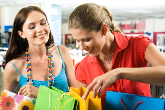 Photo of two friends looking through their shoppings with smiles in the mall