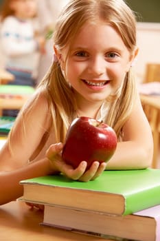 Portrait of happy pretty girl holding a red apple in the classroom