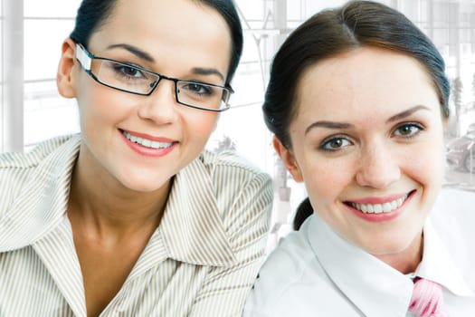 Faces of two cheerful businesswomen looking at camera with smiles