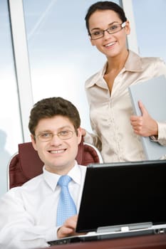 Portrait of confident boss sitting in workshop with smart businesswoman standing near by