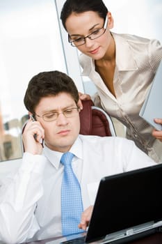 Portrait of confident boss talking by the phone with smart businesswoman standing near by