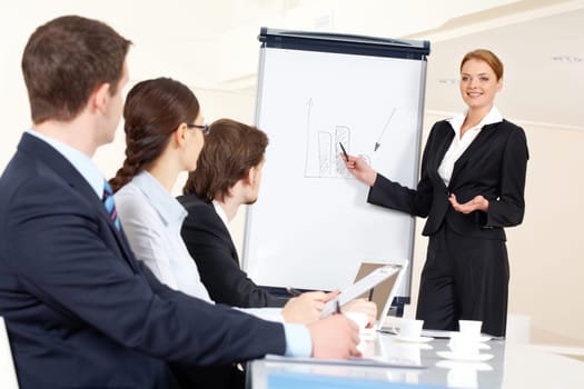 Smart and confident employee pointing at whiteboard while presenting her ideas to business partners