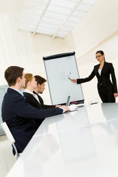 Smart and confident employee pointing at whiteboard while presenting her ideas to business partners