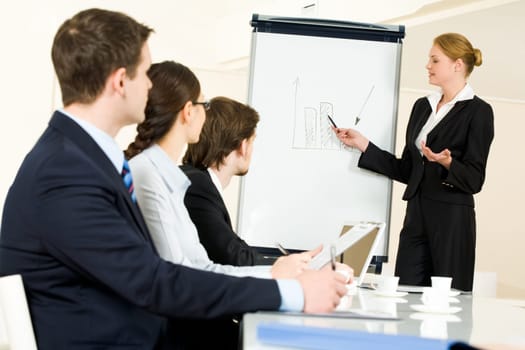 Photo of serious business people listening to female manager pointing at whiteboard while presenting new project