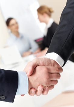 Photo of handshake of businessmen on background of communicating co-workers