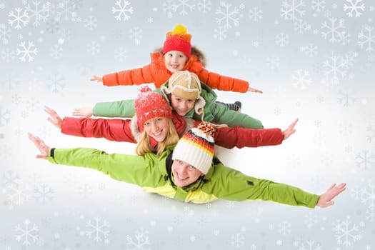 A family of four in warm clothing lying on each other with outstretched arms