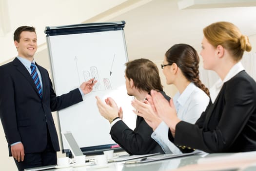 Photo of happy businessman standing by whiteboard while partners applauding to him after successful presentation