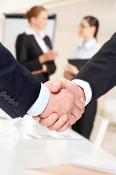 Photo of handshake of business partners after striking deal on background of communicating women