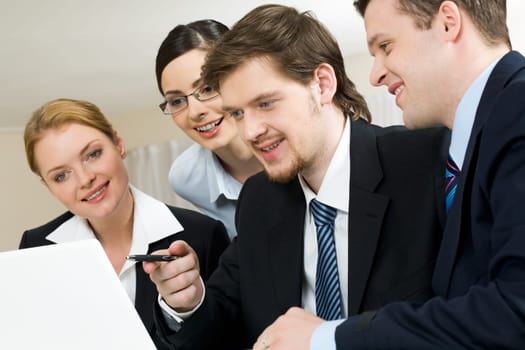 Portrait of friendly workteam looking at monitor of laptop while confident businessman pointing at screen
